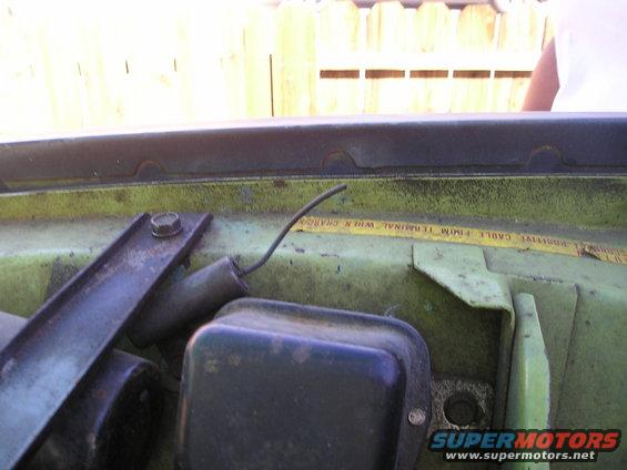 Close-up of a green engine bay with a black electrical component and a yellow warning label