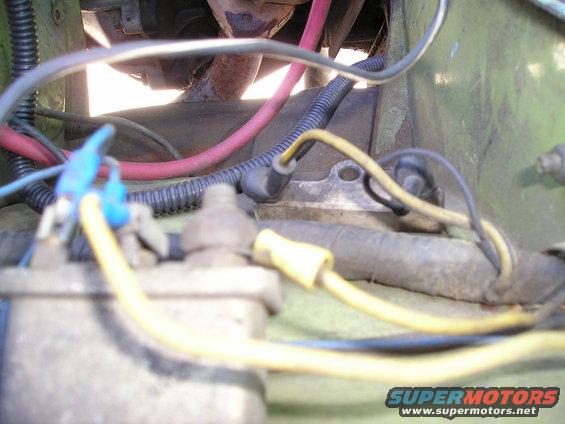 Engine bay wiring with red and yellow wires, black conduit, and rusty exhaust pipe. Green painted metal