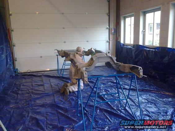 Vehicle frame on sawhorses, covered in blue tarp, inside a garage