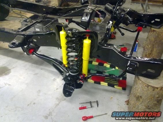 Vehicle chassis with yellow shock absorbers and black springs, undergoing repair
