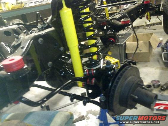 Front suspension assembly with yellow shocks and black springs, brake rotor visible