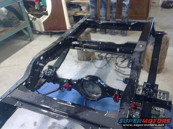 Vehicle frame and rear axle assembly, possibly undergoing restoration. Red bushings are visible on the axle