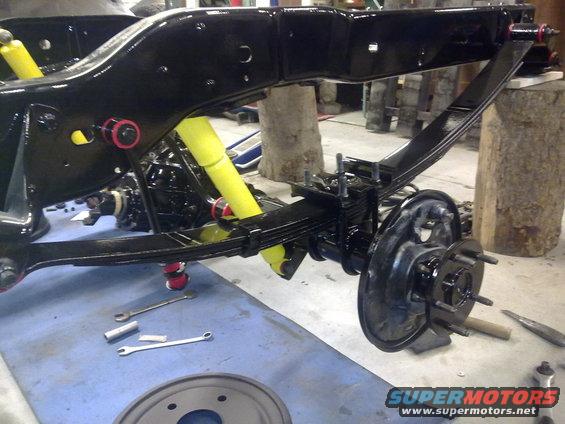 Black painted vehicle frame with yellow shocks and leaf springs, brake drum visible