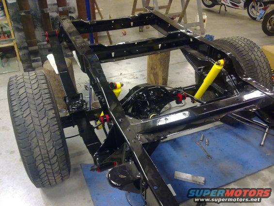 vehicle frame with rear axle, leaf springs, and yellow shocks. Tools on blue mat