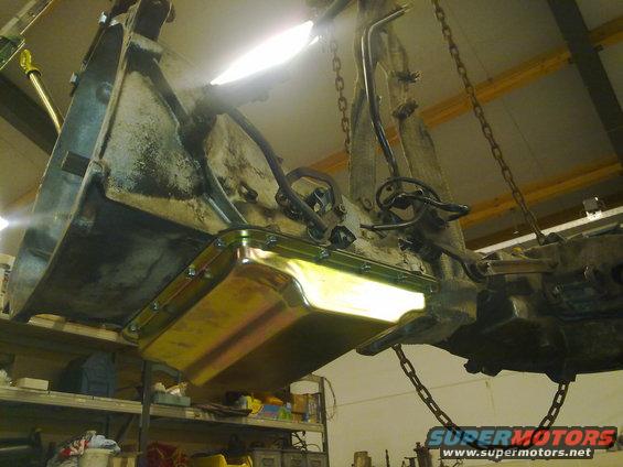 Engine oil pan and transmission assembly suspended by chains. A new gold-colored oil pan is attached