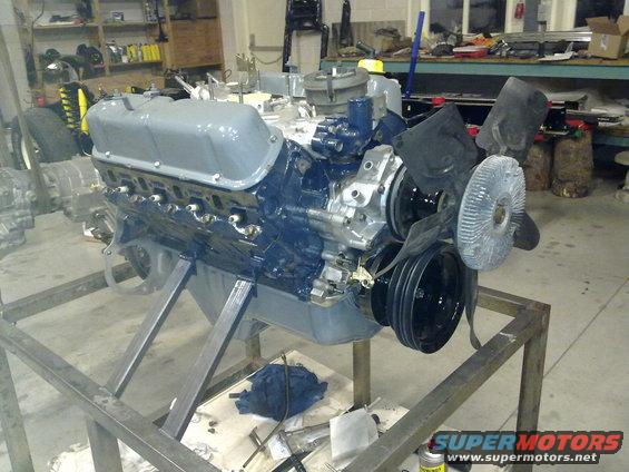 V8 engine on metal stand, painted gray and blue. Fan and pulleys visible