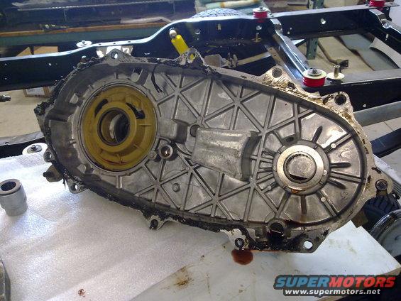 Transfer case with yellow and silver components, covered in grease and oil, resting on white padding