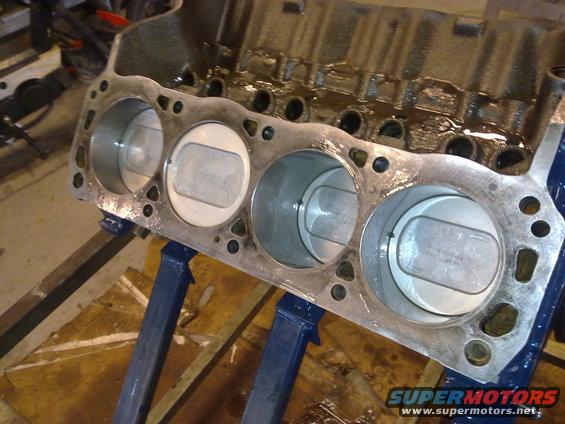 Engine block with four pistons visible, supported by blue stands