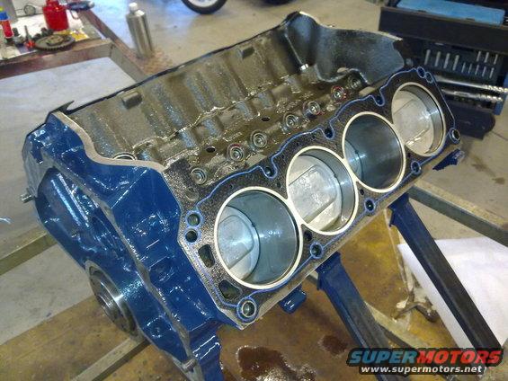 Blue engine block with pistons and gasket installed, sitting on a stand