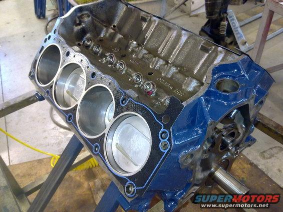 Blue painted engine block with pistons visible, on a stand