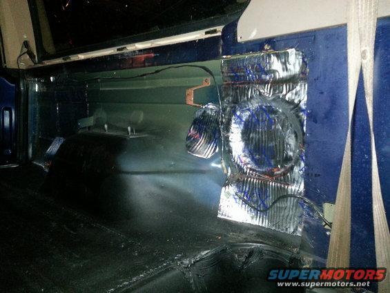 Interior rear cargo area of a blue SUV with soundproofing material on the side panel and exposed wiring