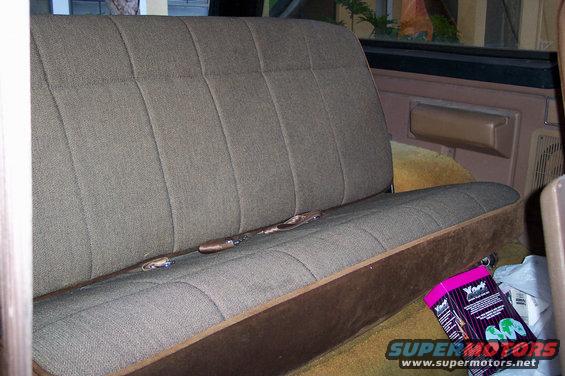 back seat with brown fabric and seatbelts, box on floor