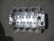 1972 Ford Ranchero - A polished aluminum V8 engine block rests on a dark asphalt surface, showing its internal cylinder bores and intake manifold bolt holes.