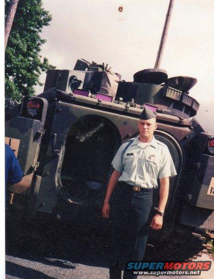 Man in military uniform standing next to a tracked military vehicle with a large cannon