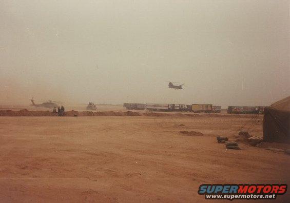 Desert scene with helicopters, a bulldozer, and train cars under a hazy sky