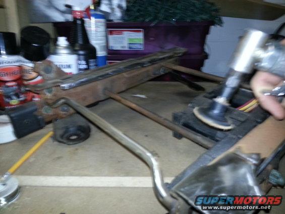Metal frame part on a workbench with a grinder being used on it. Other tools and cans are in the background