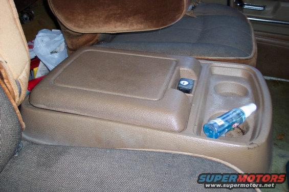 center console with cup holders and storage bin, next to car seats. Blue bottle in cup holder