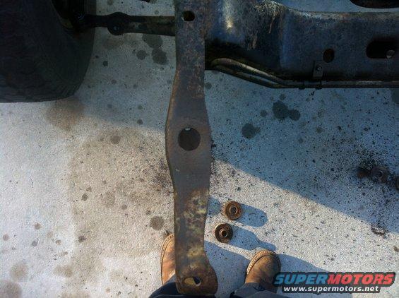 rusted metal part with holes, next to two washers on concrete floor, with tire and frame in background