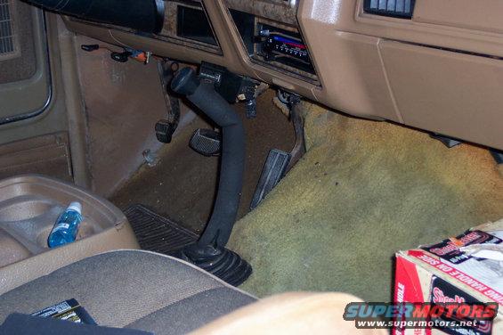 Vehicle interior with tan carpet and dashboard, floor shifter, and pedals visible