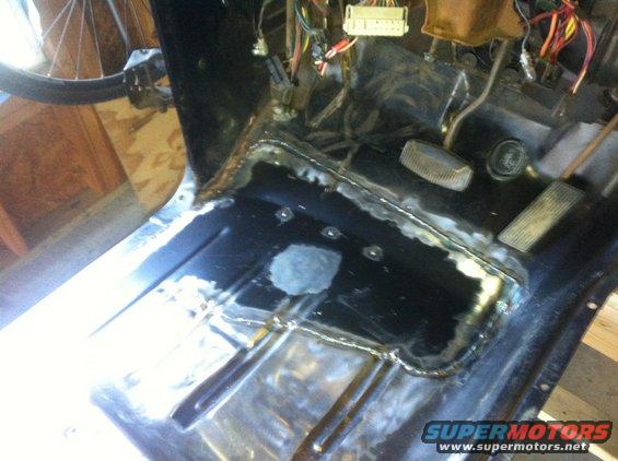 Interior floor of a vehicle undergoing repair, showing welded metal patches and exposed wiring