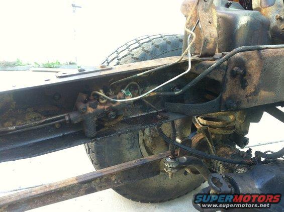 Rusty vehicle frame with brake lines and suspension parts visible, tire in background