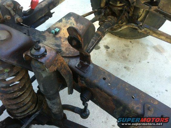 Rusted vehicle frame with suspension parts, shock absorber, and coil spring visible