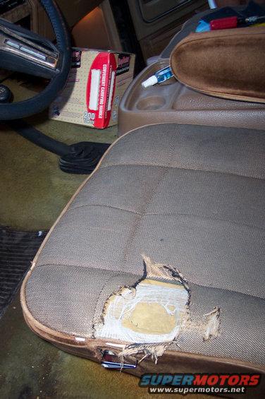 Torn driver's seat in a vehicle interior, with a box of tissues and a spray bottle visible