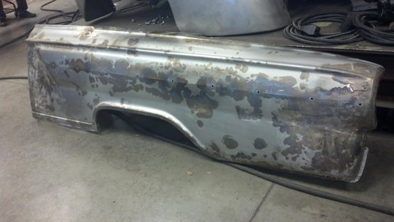 Bare metal car fender with rust spots and drill holes