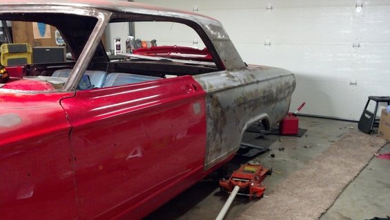 Red and bare metal 1964 Ford Fairlane coupe body, jacked up, in a garage