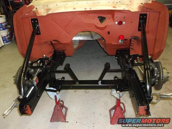 Car chassis on jack stands, showing front suspension and subframe. Red primer on firewall