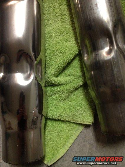Two dented exhaust pipes, one shiny and one dull, resting on a green towel