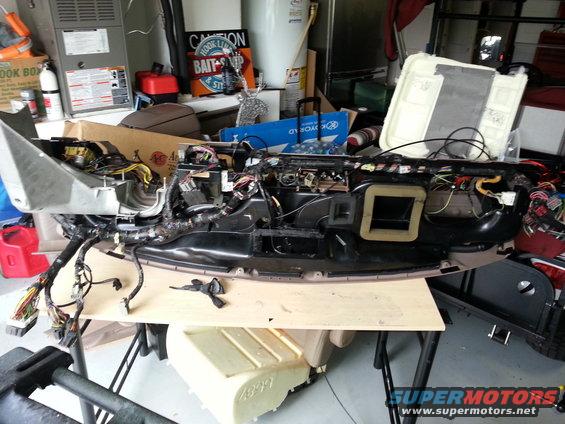 Disassembled dashboard assembly with exposed wiring and components, resting on a table