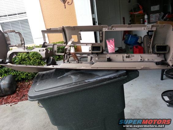 Tan dashboard assembly removed from a vehicle, resting on a trash bin