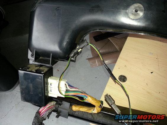 Close-up of a vehicle's interior wiring harness with a black box and many colored wires connected to a white connector labeled 'WCM'