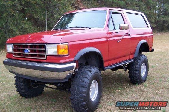 Red lifted Ford Bronco with large off-road tires parked on grass