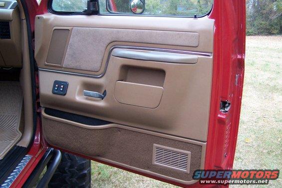 Red Ford Bronco interior door panel with tan trim, power window controls, and speaker grille