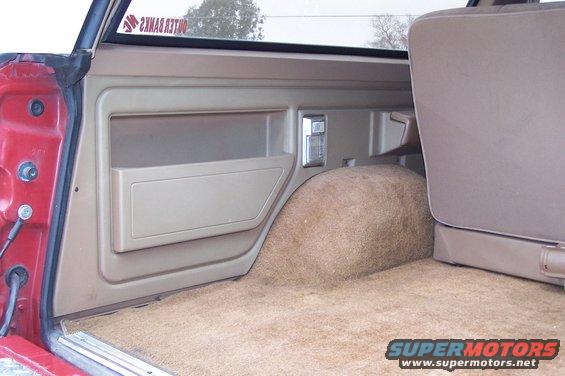 Interior of a vehicle's cargo area, showing tan carpet and door panel with a storage compartment