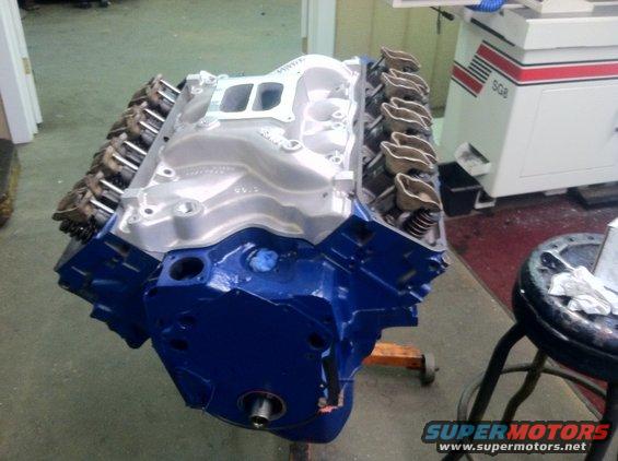 Blue engine block with silver intake manifold and valve covers, mounted on an orange engine stand