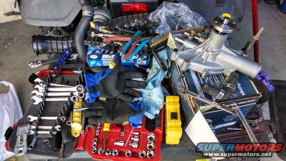 Pile of tools and a new water pump on top of an engine bay