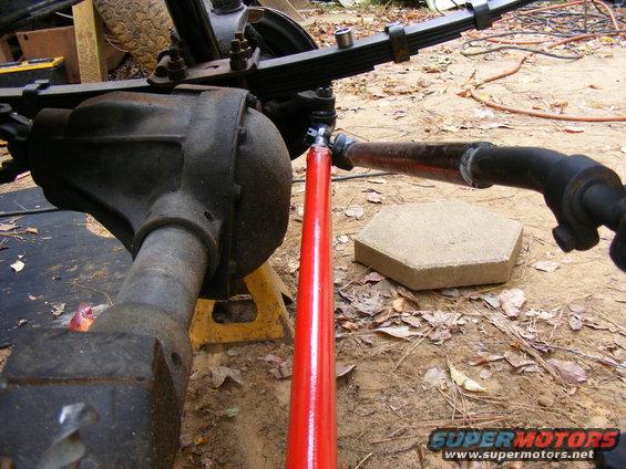 Close-up of a vehicle's rear axle assembly with leaf springs and a red shock absorber. The vehicle is on jack stands outdoors
