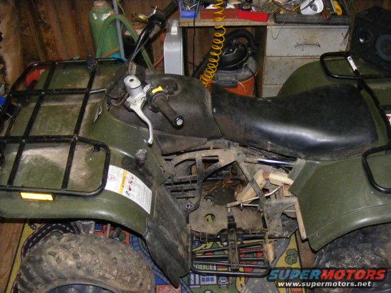 Green ATV with black racks, parked indoors. Some parts are exposed