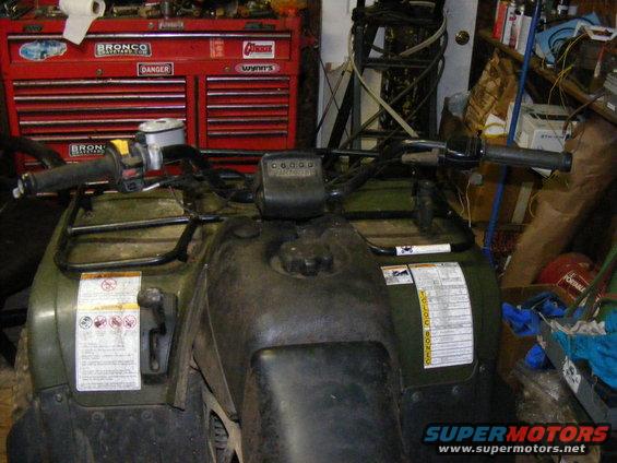 Green ATV dashboard with handlebars and a red toolbox in the background