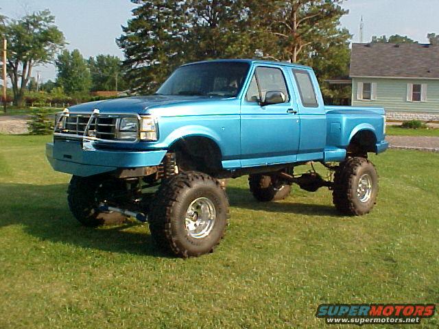 Blue 1992 Ford F-150 truck with large tires and lifted suspension, parked on grass