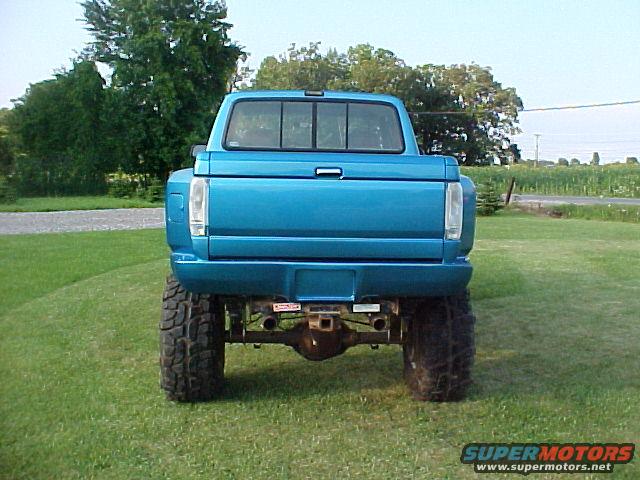 1992 Ford F-150 pickup truck, rear view, lifted with large tires, blue paint, grass background