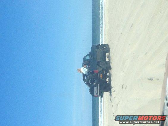 Black SUV parked on a sandy beach near the ocean with a person inside