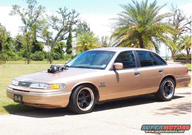 Gold 1993 Ford Crown Victoria with hood scoop and custom wheels parked outside