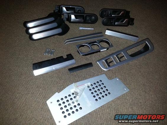 Car interior trim pieces including door handles, window switch surrounds, and a center console trim piece with cup holders