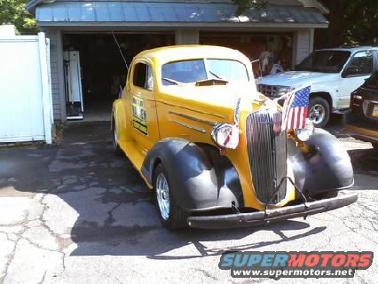 Yellow 1935 Chevrolet coupe with black fenders and an American flag on the grille