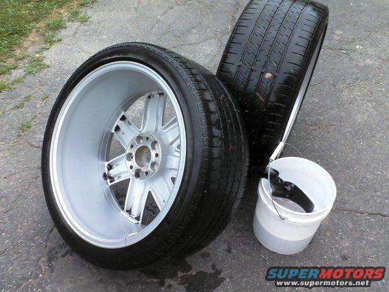 Two car wheels with tires and a bucket of water on the ground