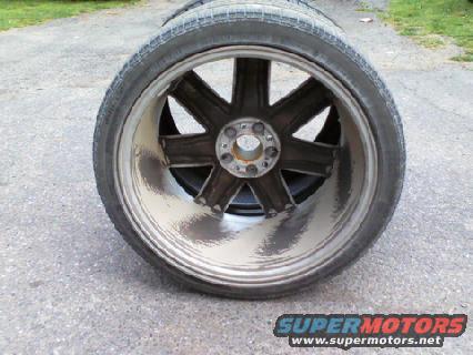Wheel and tire assembly, close-up side view, showing a dark multi-spoke rim with a silver lip and a worn tire